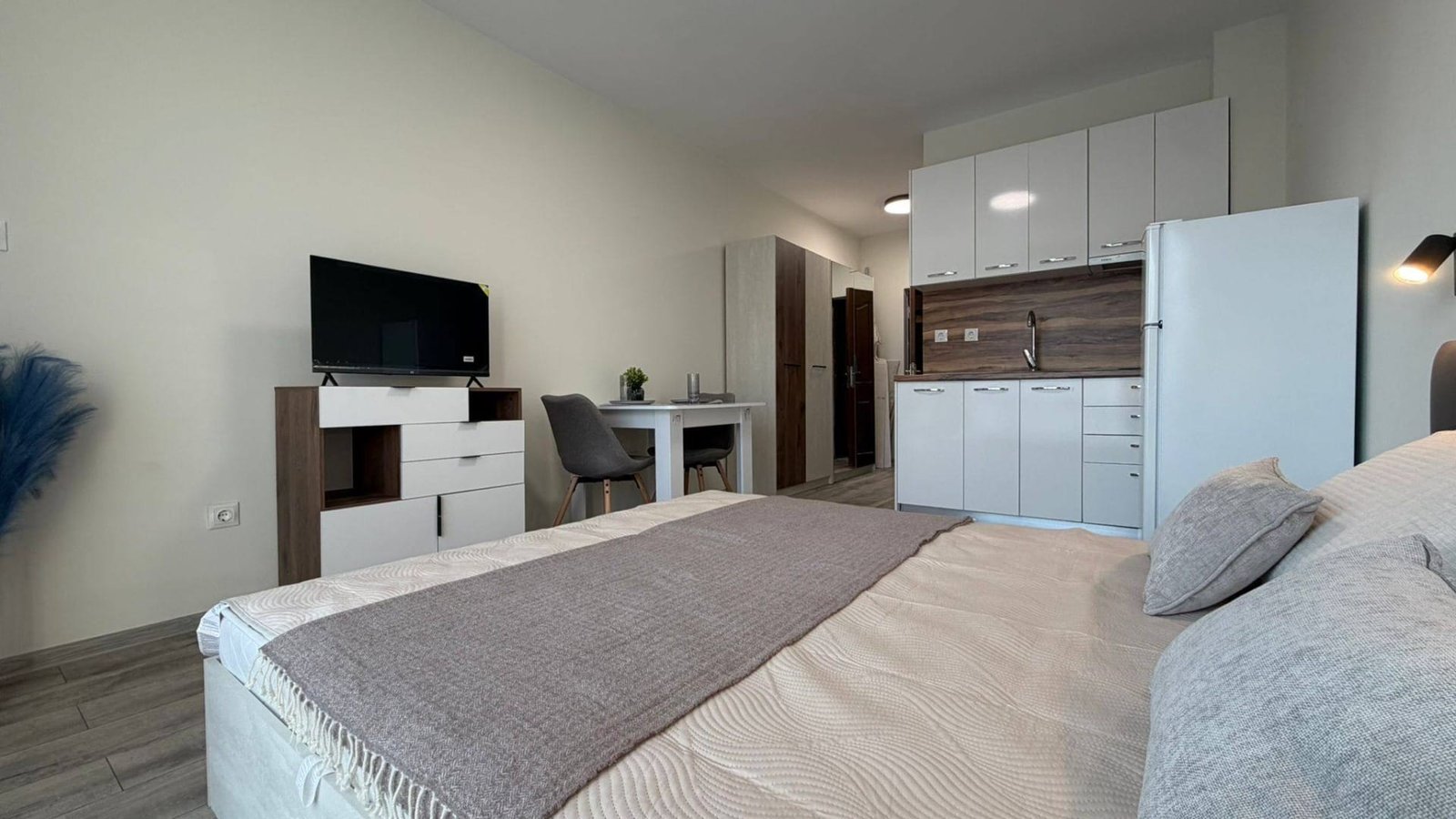 Современная однокомнатная квартира в Болгарии с кухней, кроватью, телевизором и столом, идеально подходит для комфортного проживания.