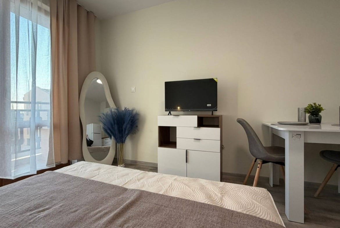 Современная квартира в Болгарии с теплым интерьером, телевизором, столом и зеркалом, идеальная для аренды или покупки.