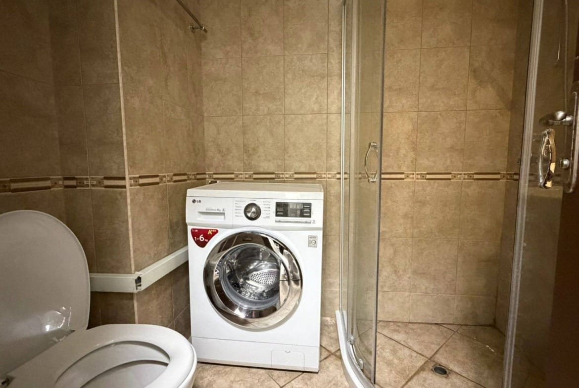 Современная ванная комната с душевой кабиной, стиральной машиной и керамической плиткой в нейтральных тонах.