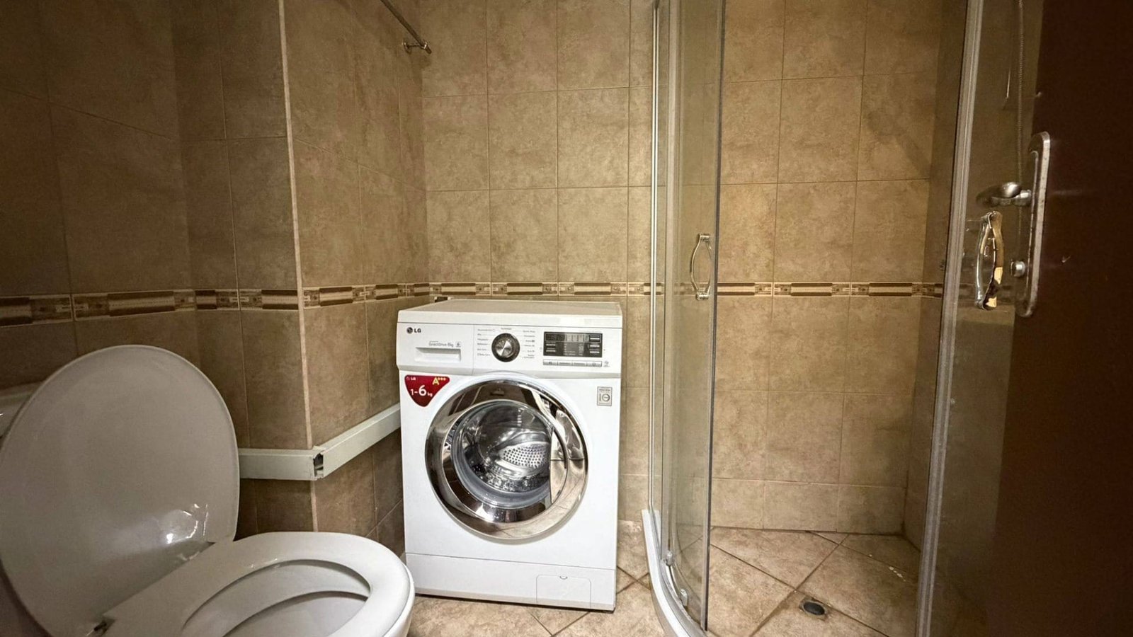 Современная ванная комната с душевой кабиной, стиральной машиной и керамической плиткой в нейтральных тонах.