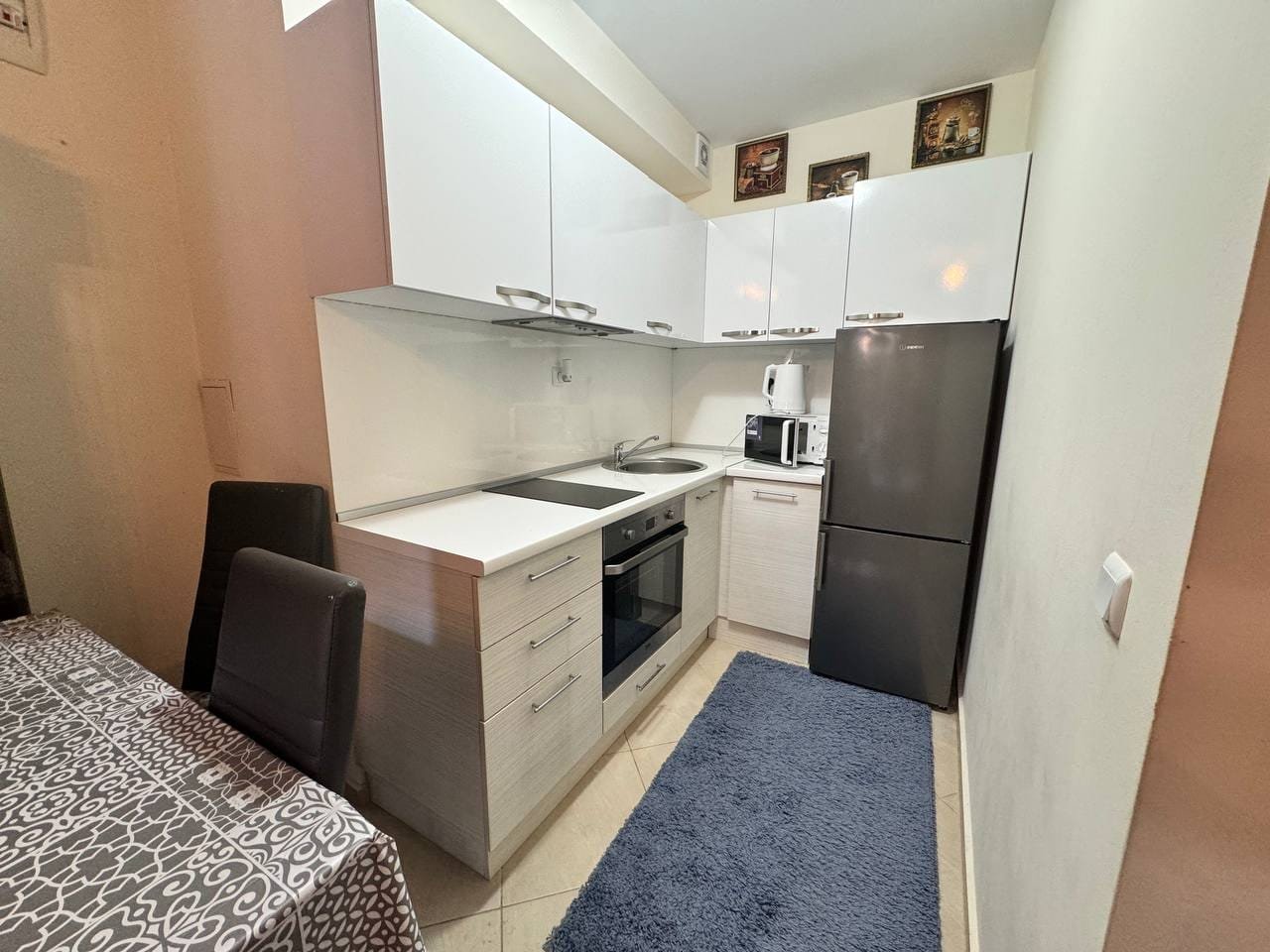 Современная кухня с белыми фасадами, плитой, холодильником и столом для продажи недвижимости в Болгарии.