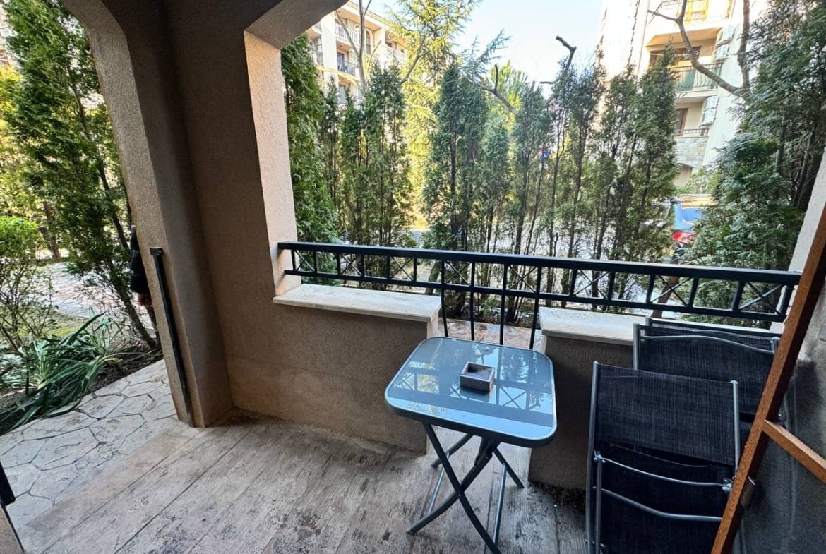 Балкон с небольшой столик и стульями, окружённый зелёными растениями, идеальное место для отдыха при продаже недвижимости в Болгарии.