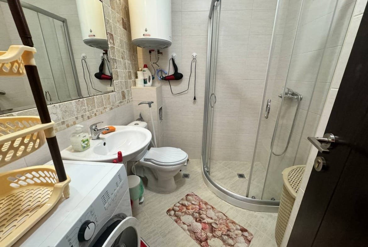 Современная ванная комната с душевой кабиной, унитазом и стиральной машиной, оформленная в светлых тонах.