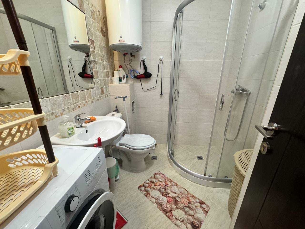 Современная ванная комната с душевой кабиной, унитазом и стиральной машиной, оформленная в светлых тонах.