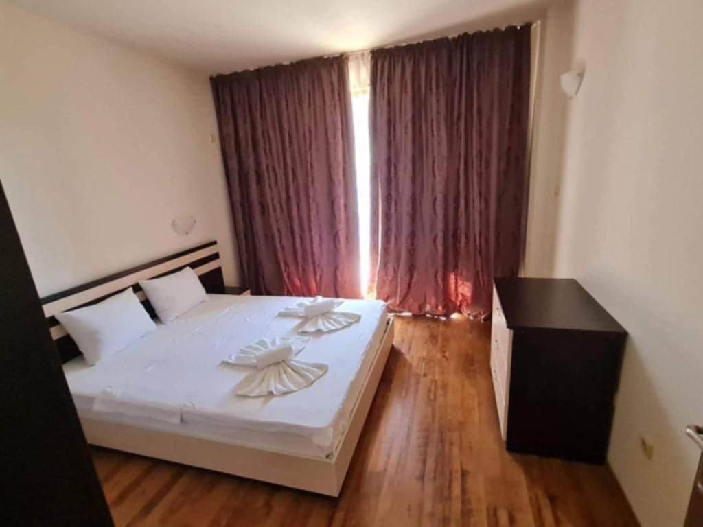 Современная спальня с двуспальной кроватью, витражными шторами и деревянным полом, идеально подходящая для отдыха в Болгарии.