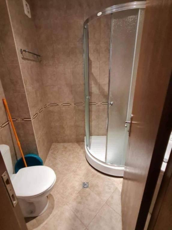 Современная ванная комната с душевой кабинкой, унитазом и чистящими принадлежностями, оформленная в нейтральных тонах.