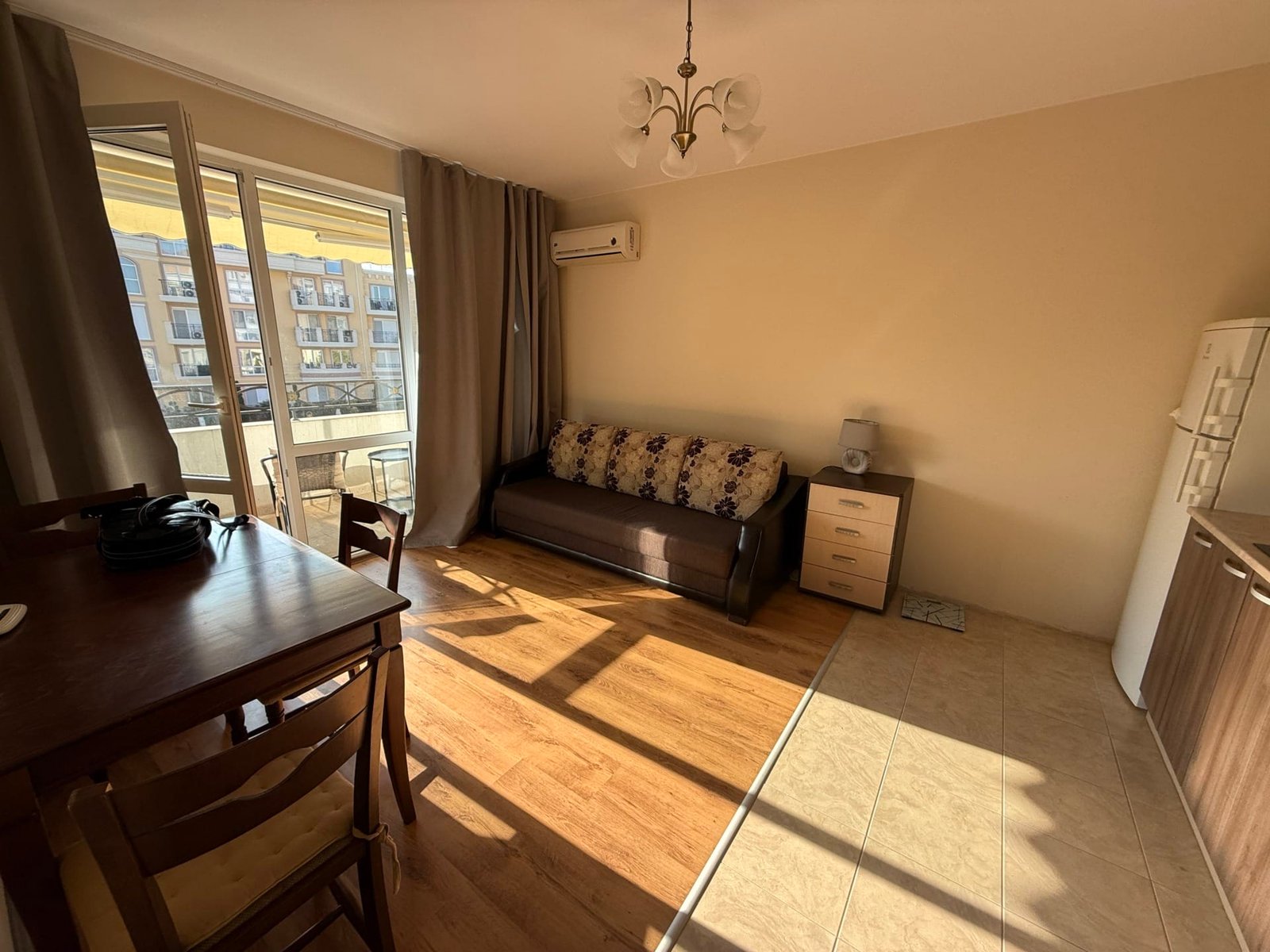 Светлая жилая комната с диваном, обеденным столом и кухонным уголком, идеальная для покупки недвижимости в Болгарии.