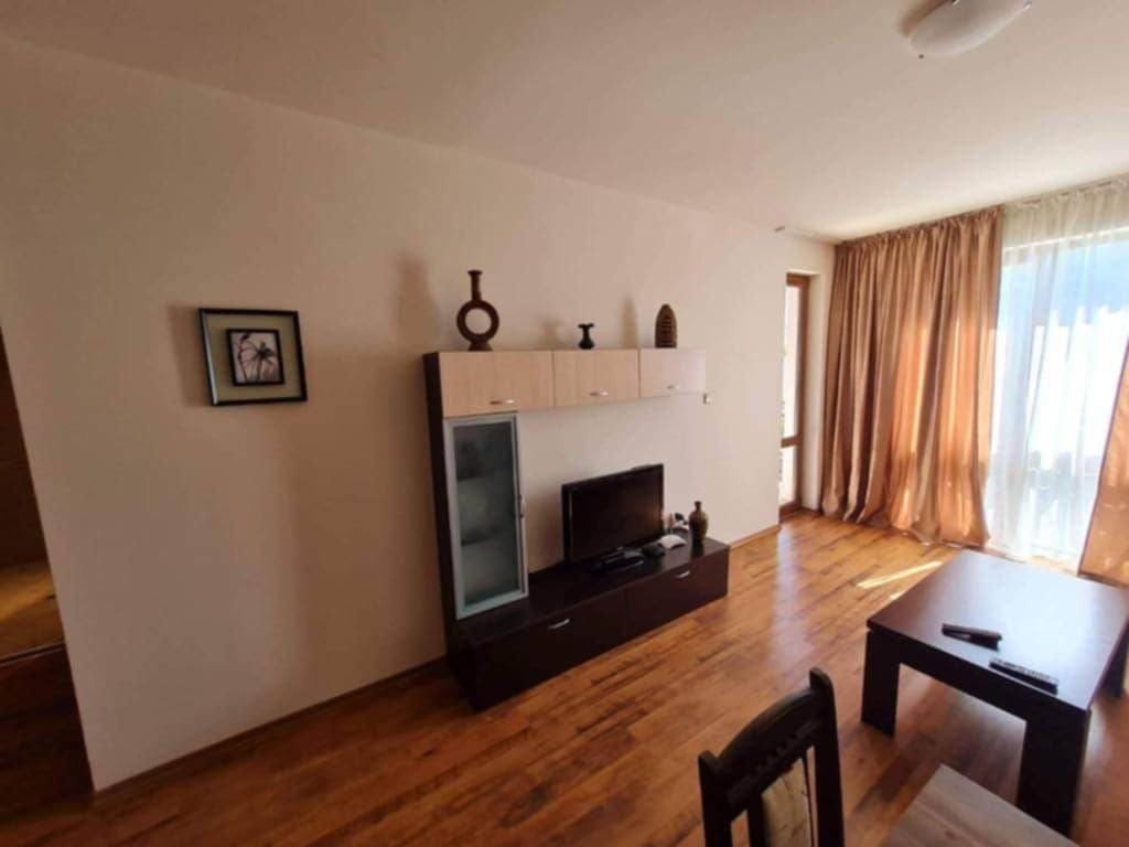 Современный интерьер квартиры в Болгарии с деревянным полом, мебелью и большим окном, обеспечивающим естественное освещение.