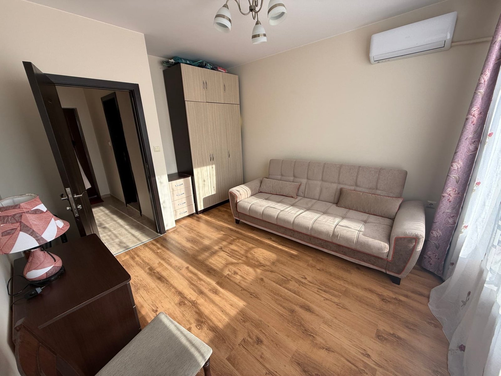 Комфортная квартира в Болгарии, светлая комната с диваном, шкафом и кондиционером, идеальная для продажи или аренды.