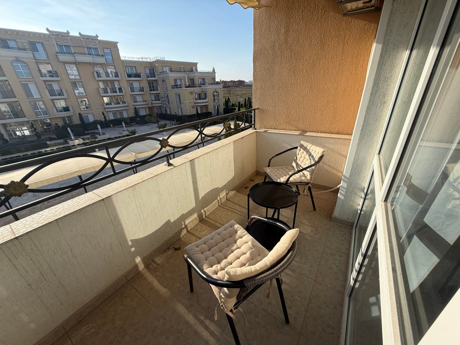 Балкон с двумя креслами, светлые тона, вид на жилой комплекс в Болгарии, отражающий комфортные условия для жизни.