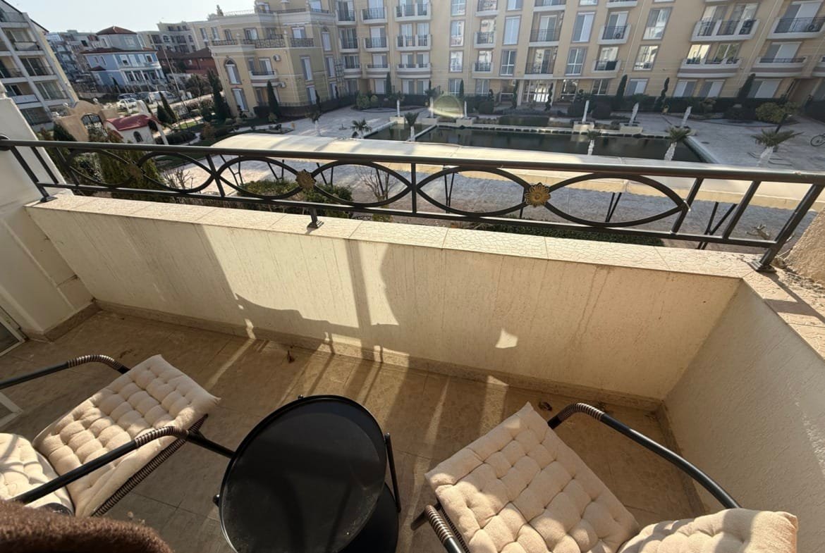 Балкон с двумя креслами и столиком, открывающий вид на жилой комплекс в Болгарии, идеальное место для отдыха и наслаждения.