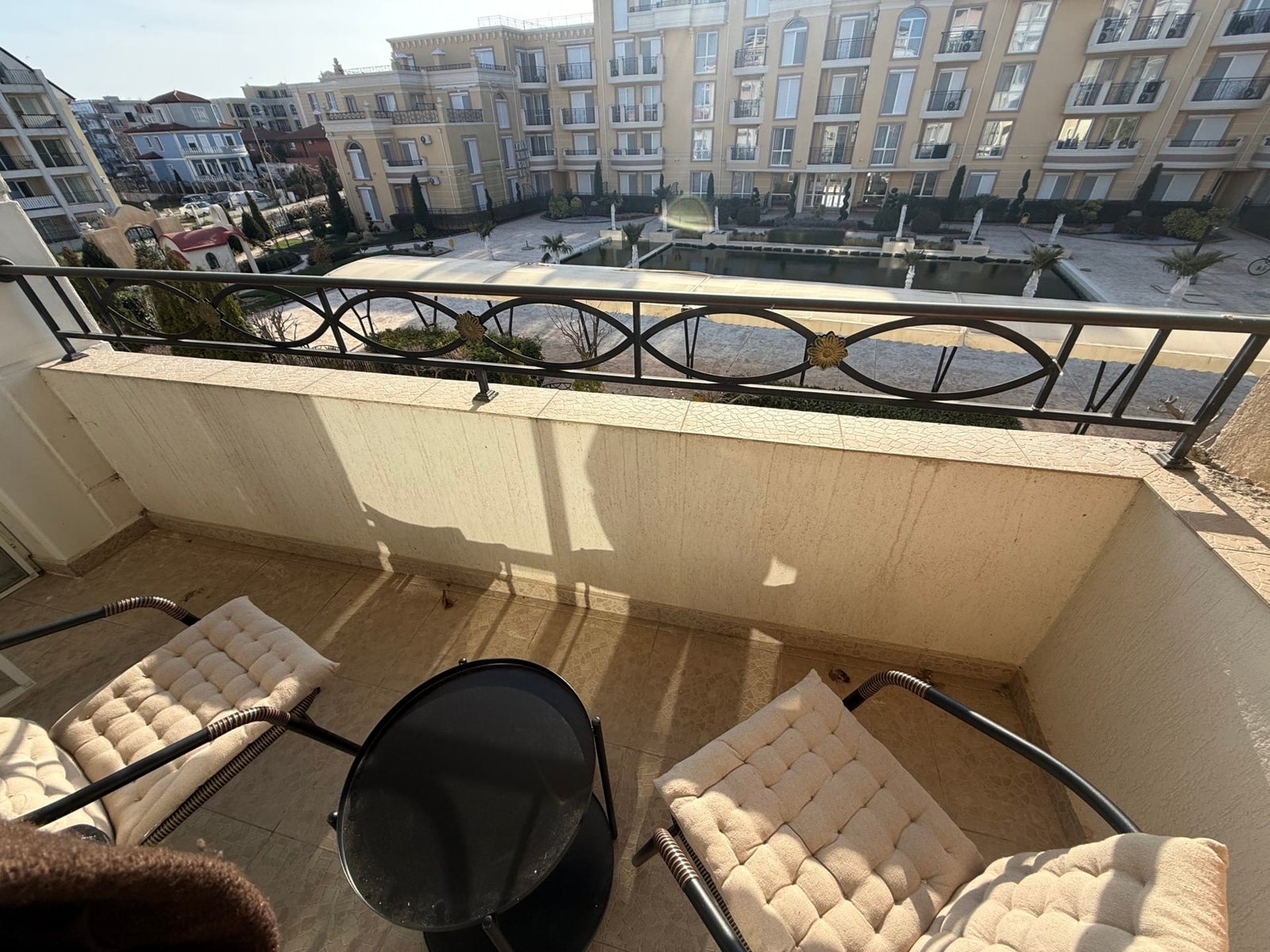 Балкон с двумя креслами и столиком, открывающий вид на жилой комплекс в Болгарии, идеальное место для отдыха и наслаждения.