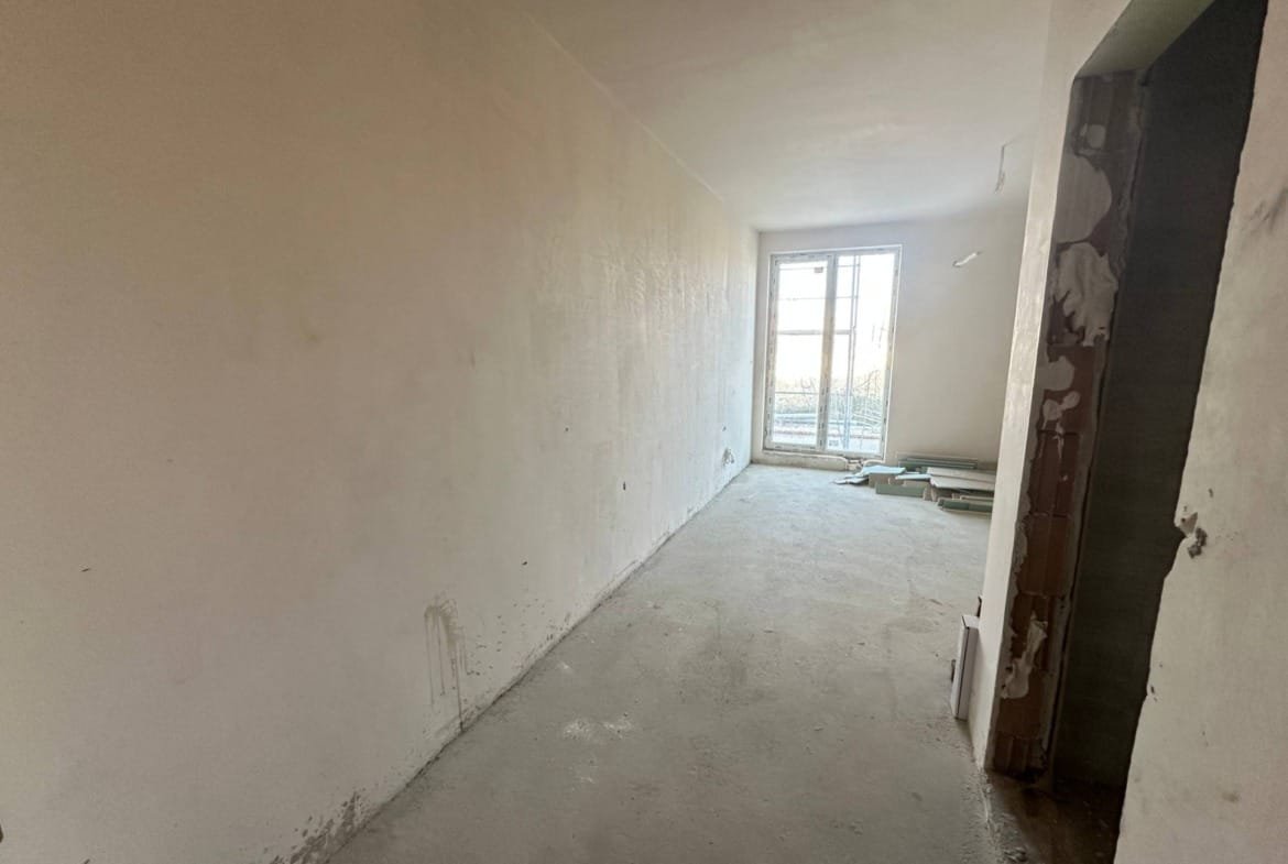 Пустое помещение с белыми стенами и бетонным полом, окно с видом на улицу, подготовлено для дальнейшей отделки.