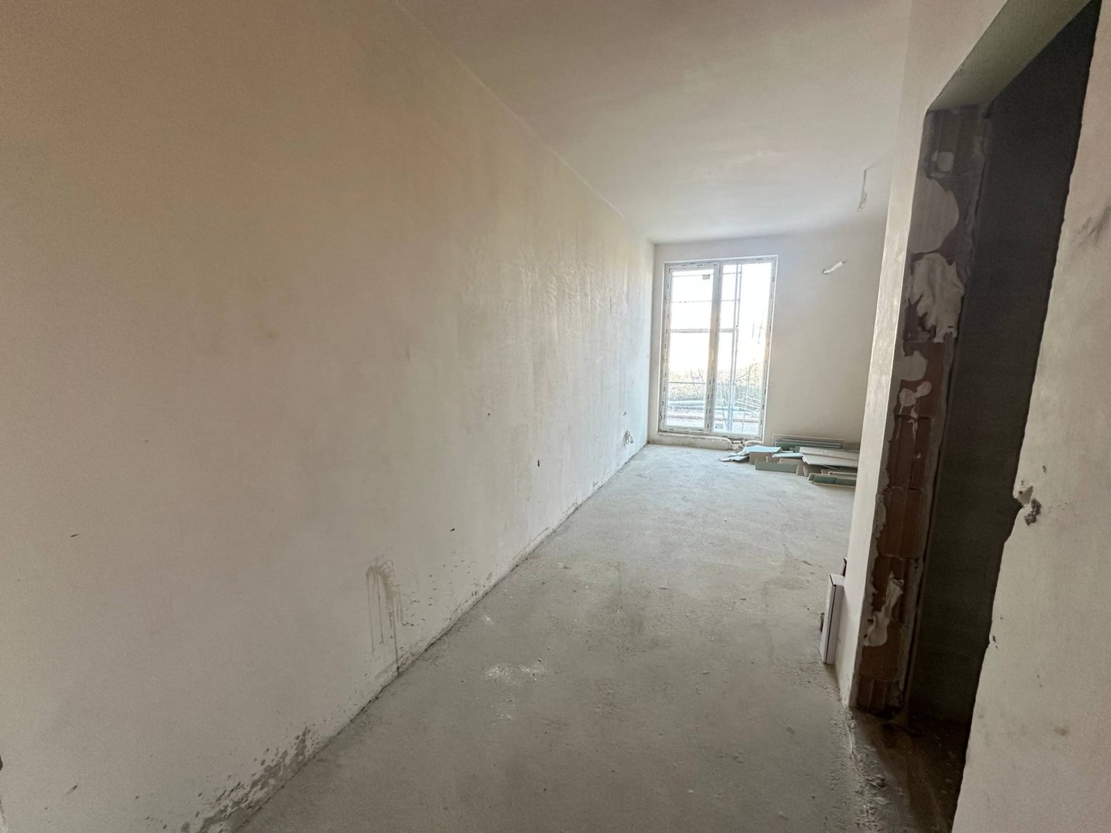 Пустое помещение с белыми стенами и бетонным полом, окно с видом на улицу, подготовлено для дальнейшей отделки.