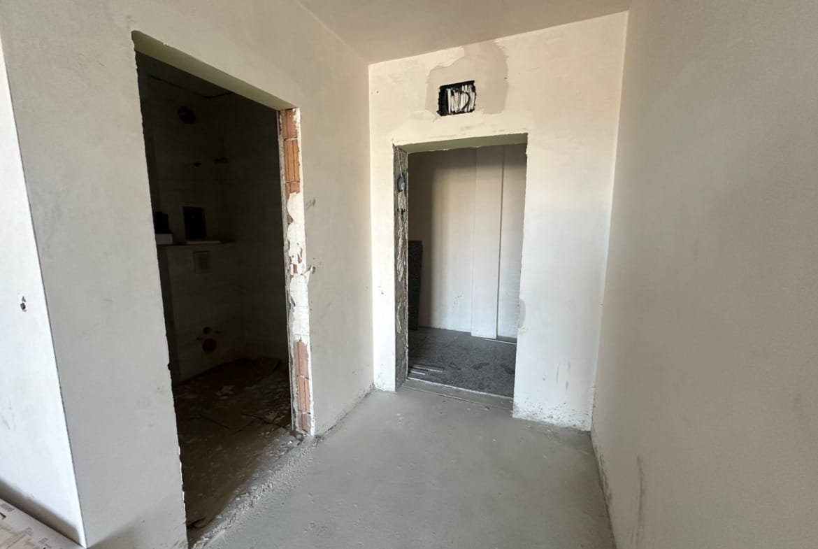 Пустое помещение с бетонными стенами, дверными проемами и незавершенной отделкой, готовое для внутренней отделки.