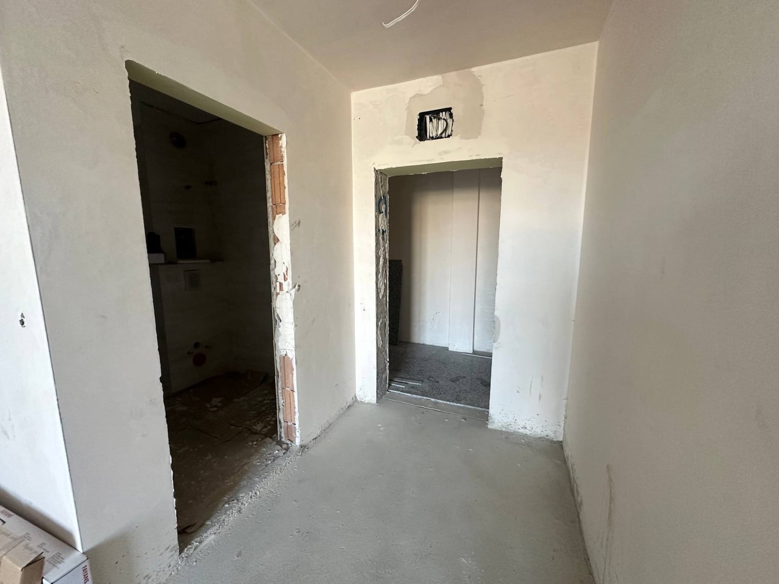 Пустое помещение с бетонными стенами, дверными проемами и незавершенной отделкой, готовое для внутренней отделки.