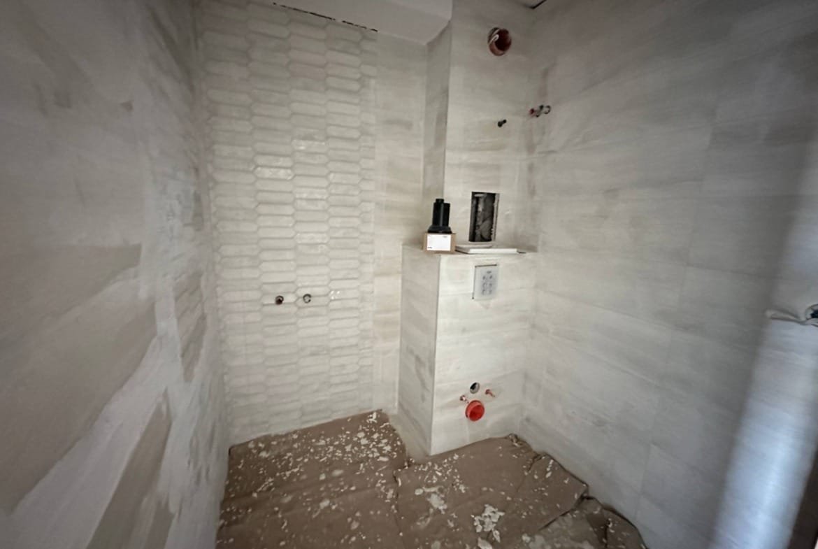 Современная ванная комната в стадии ремонта с белыми стенами и плиткой, расположенная в комплексе “La Mer Gold”.