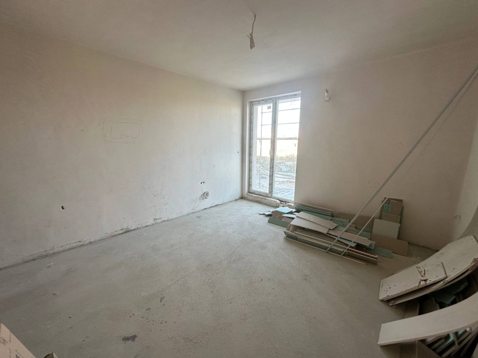 Светлое пустое помещение с окном, необработанные стены и строительные материалы на полу. Подходит для студии в "La Mer Gold".