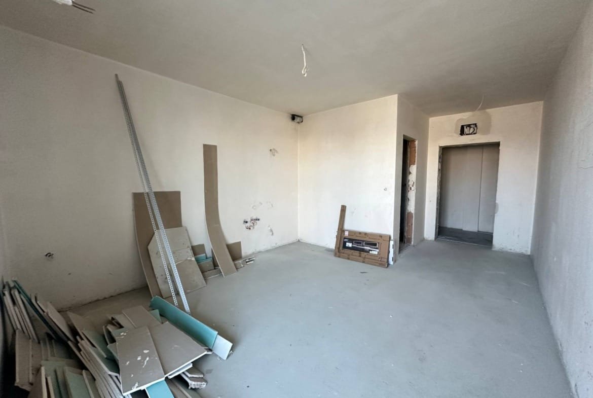 Пустое помещение в комплексе La Mer Gold, строительные материалы и оборудование в углу, стены без отделки.