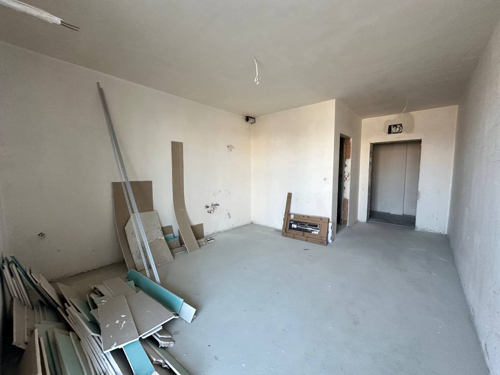 Пустое помещение в комплексе La Mer Gold, строительные материалы и оборудование в углу, стены без отделки.