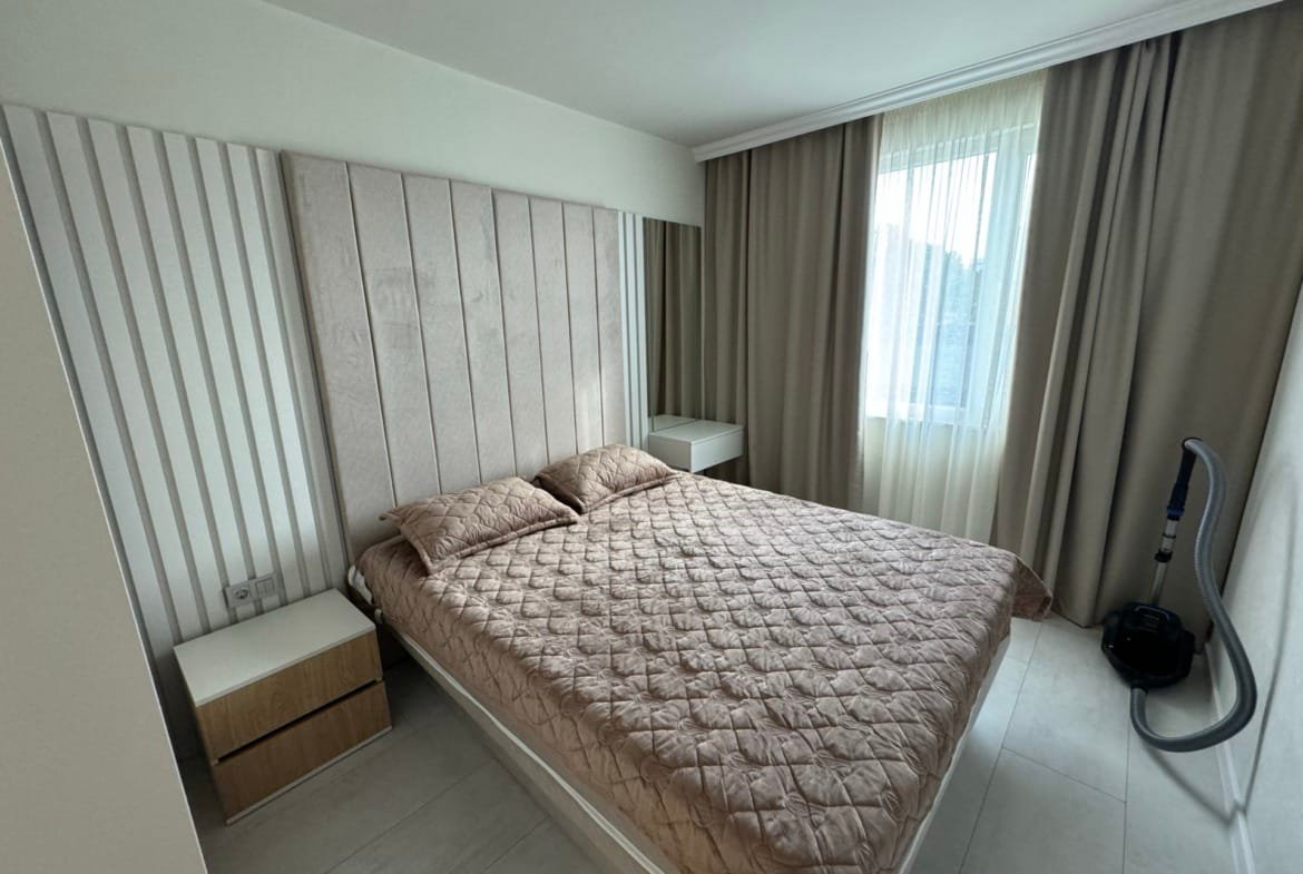 Современная спальня с двуспальной кроватью, светлыми шторами и минималистичной мебелью для продажи в Болгарии.