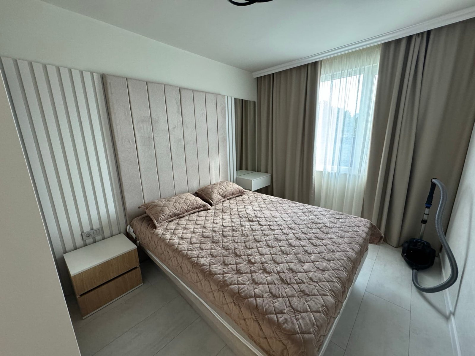 Современная спальня с двуспальной кроватью, светлыми шторами и минималистичной мебелью для продажи в Болгарии.