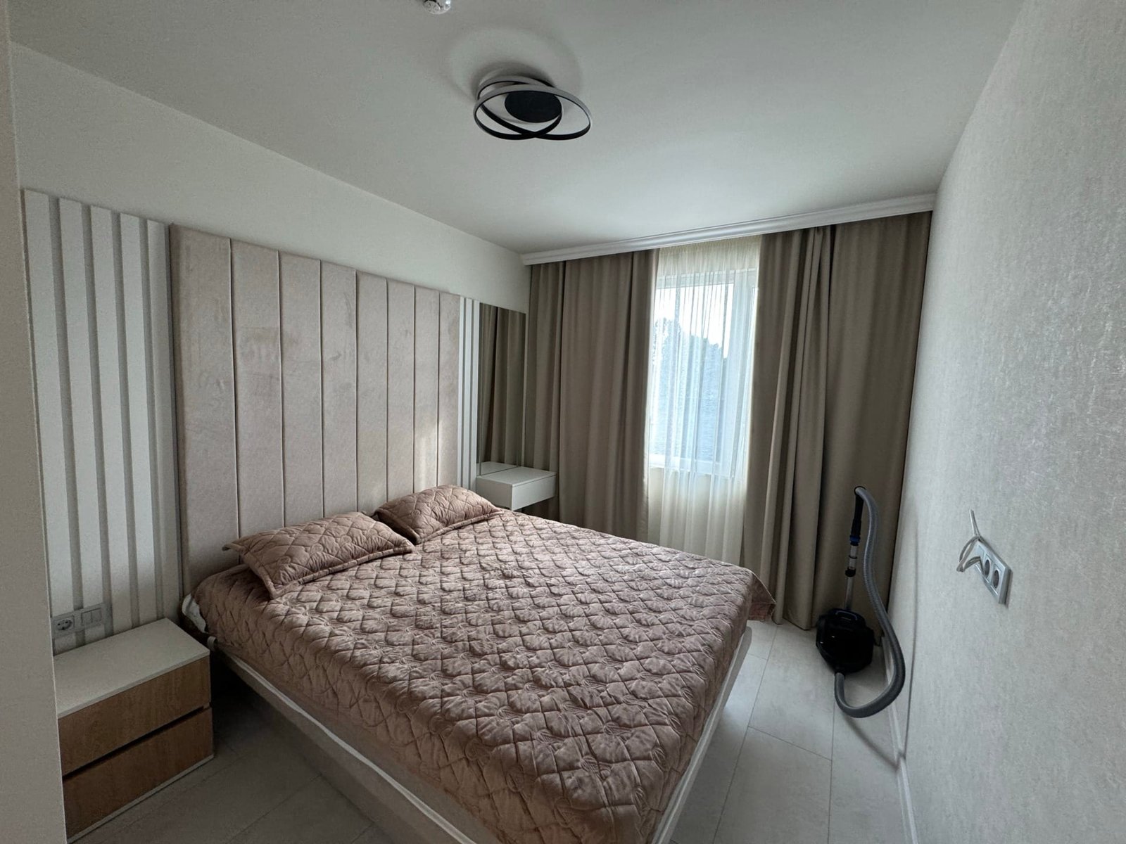 Современно оформленная спальня с двуспальной кроватью, мягкими тонами и окнами, добавляющими естественный свет.