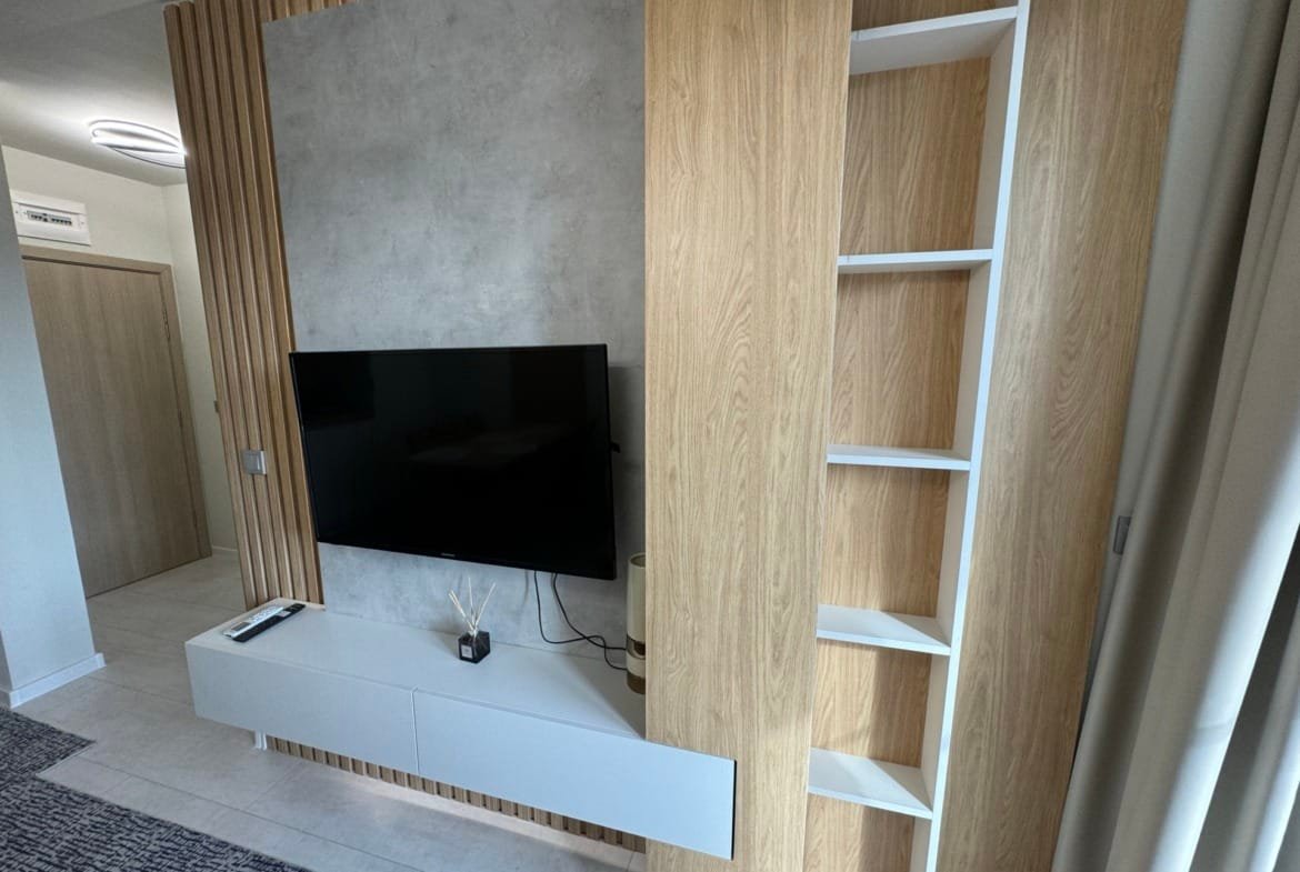 Современный гостиный уголок с телевизором, деревянными элементами и минималистичной мебелью, подходящий для покупки недвижимости в Болгарии.