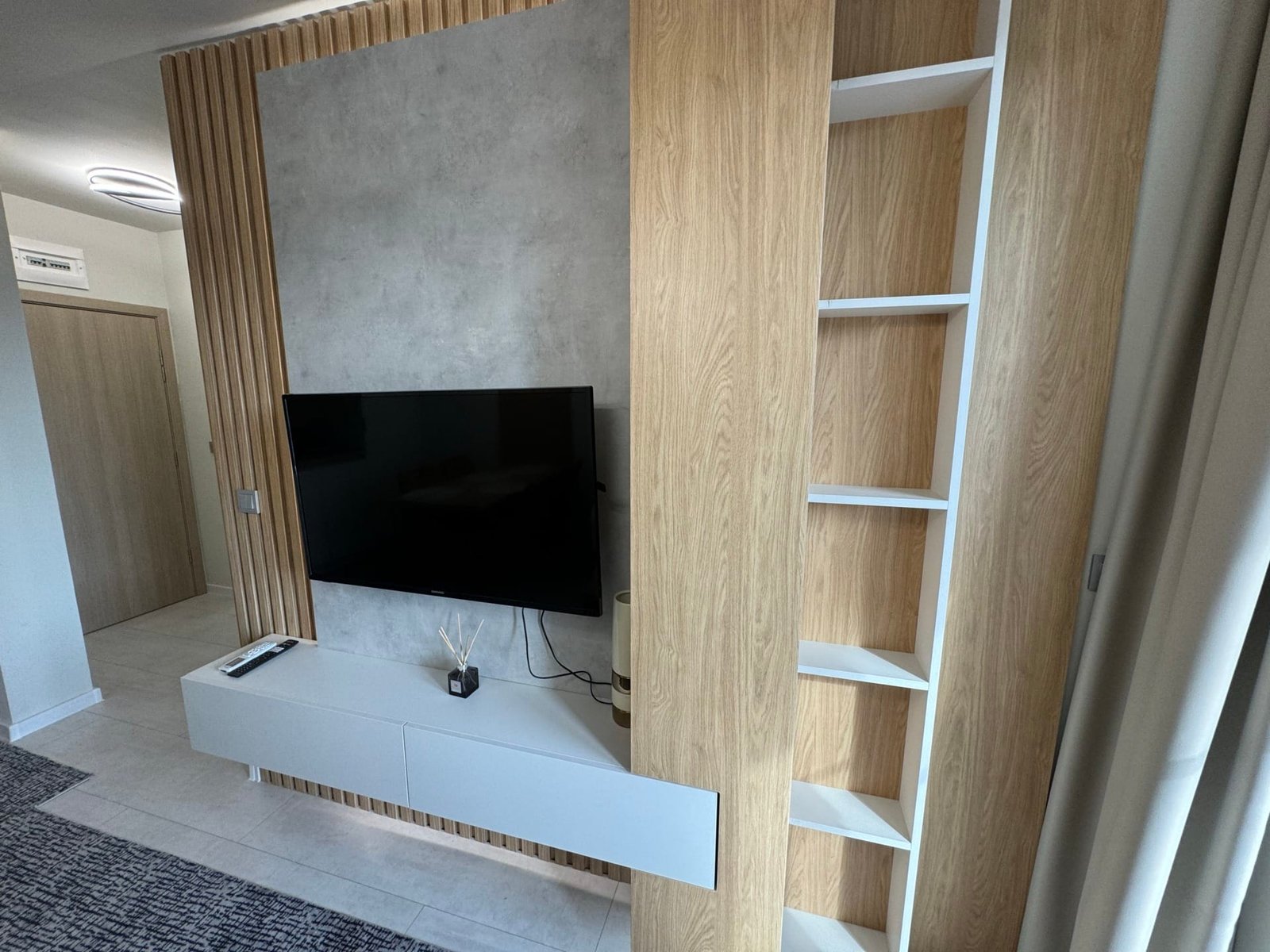 Современный гостиный уголок с телевизором, деревянными элементами и минималистичной мебелью, подходящий для покупки недвижимости в Болгарии.