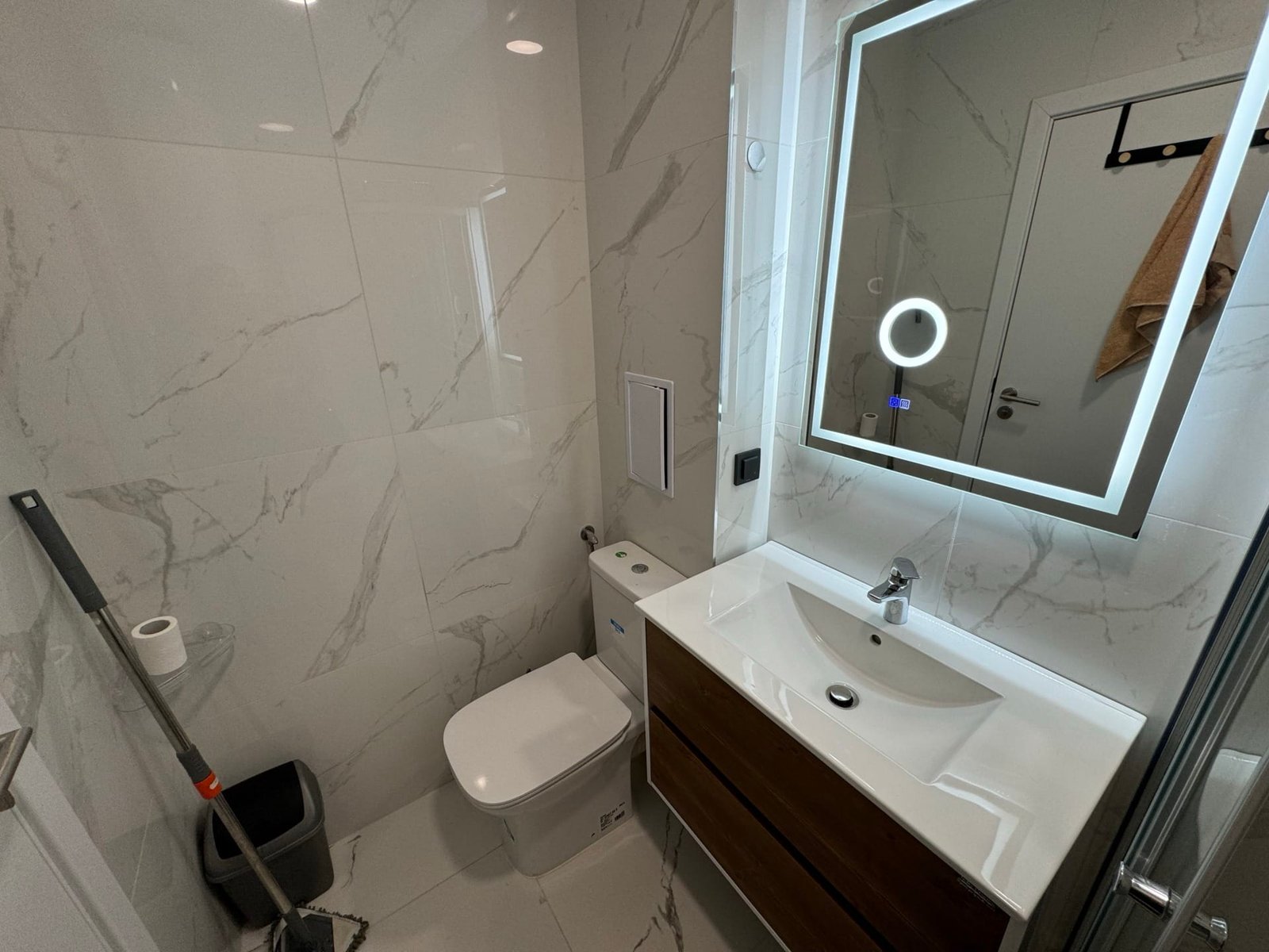 Современный санузел с белой плиткой, стильным зеркалом и сантехникой, подходящий для продажи недвижимости в Болгарии.