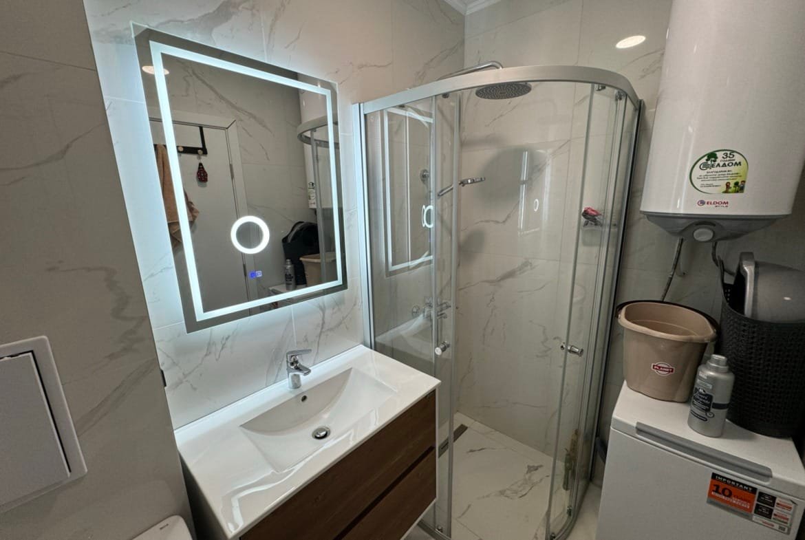 Современная ванная комната с зеркалом, душевой кабиной и стильно оформленной сантехникой для продажи недвижимости в Болгарии.