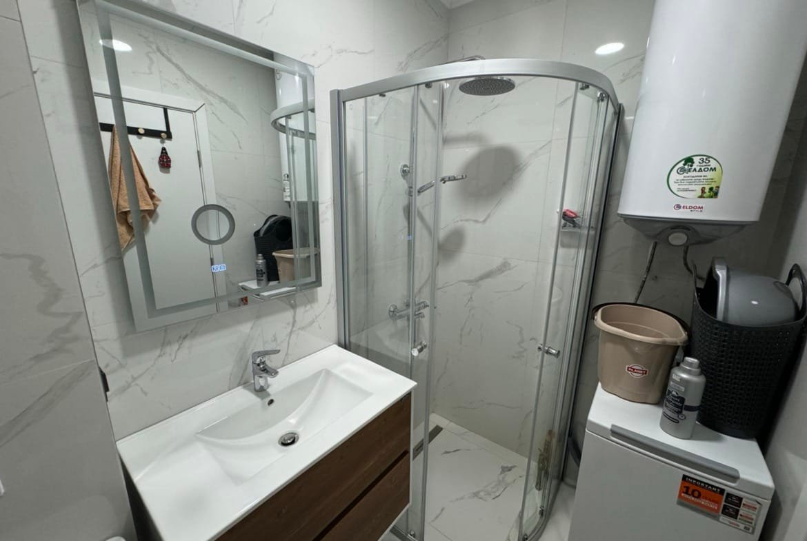 Современная ванная комната с душевой кабиной, умывальником, зеркалом и стиральной машиной, подходящая для покупки недвижимости в Болгарии.