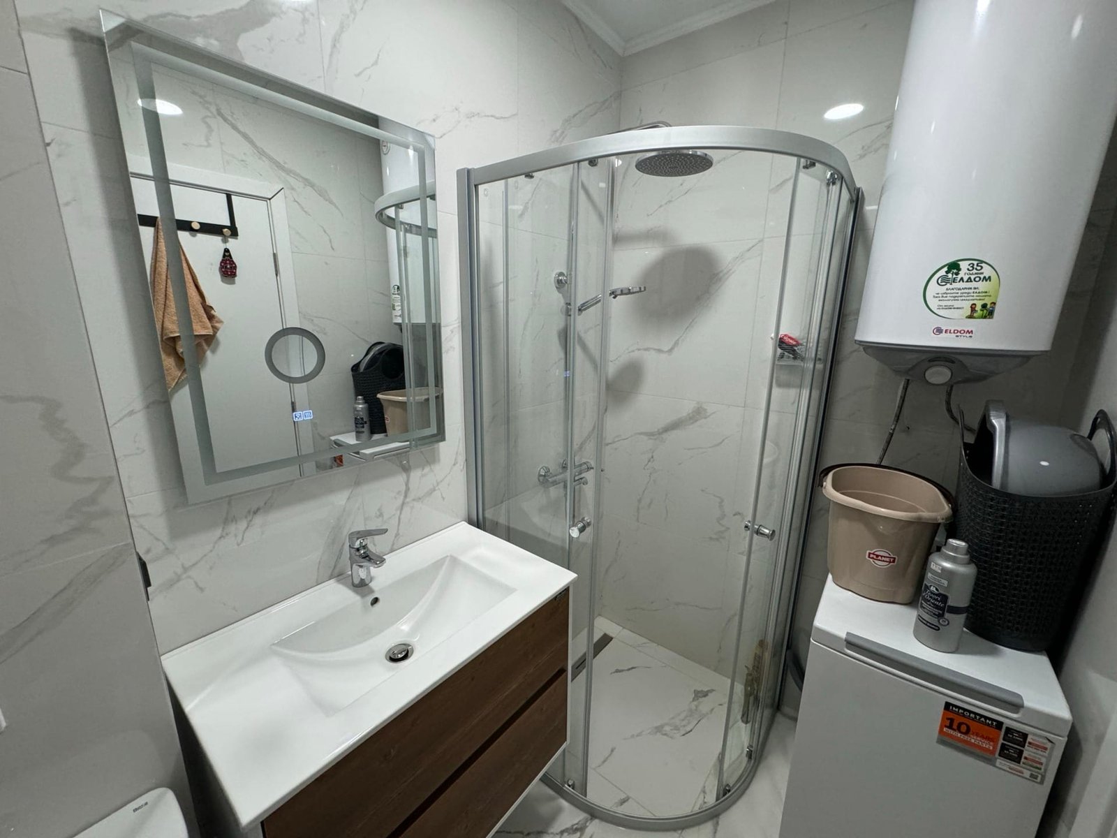 Современная ванная комната с душевой кабиной, умывальником, зеркалом и стиральной машиной, подходящая для покупки недвижимости в Болгарии.