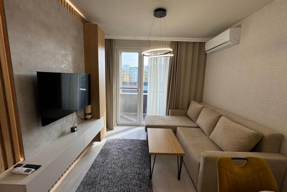 Современный интерьер квартиры с диваном, телевизором и балконом, идеальной для покупки недвижимости в Болгарии.