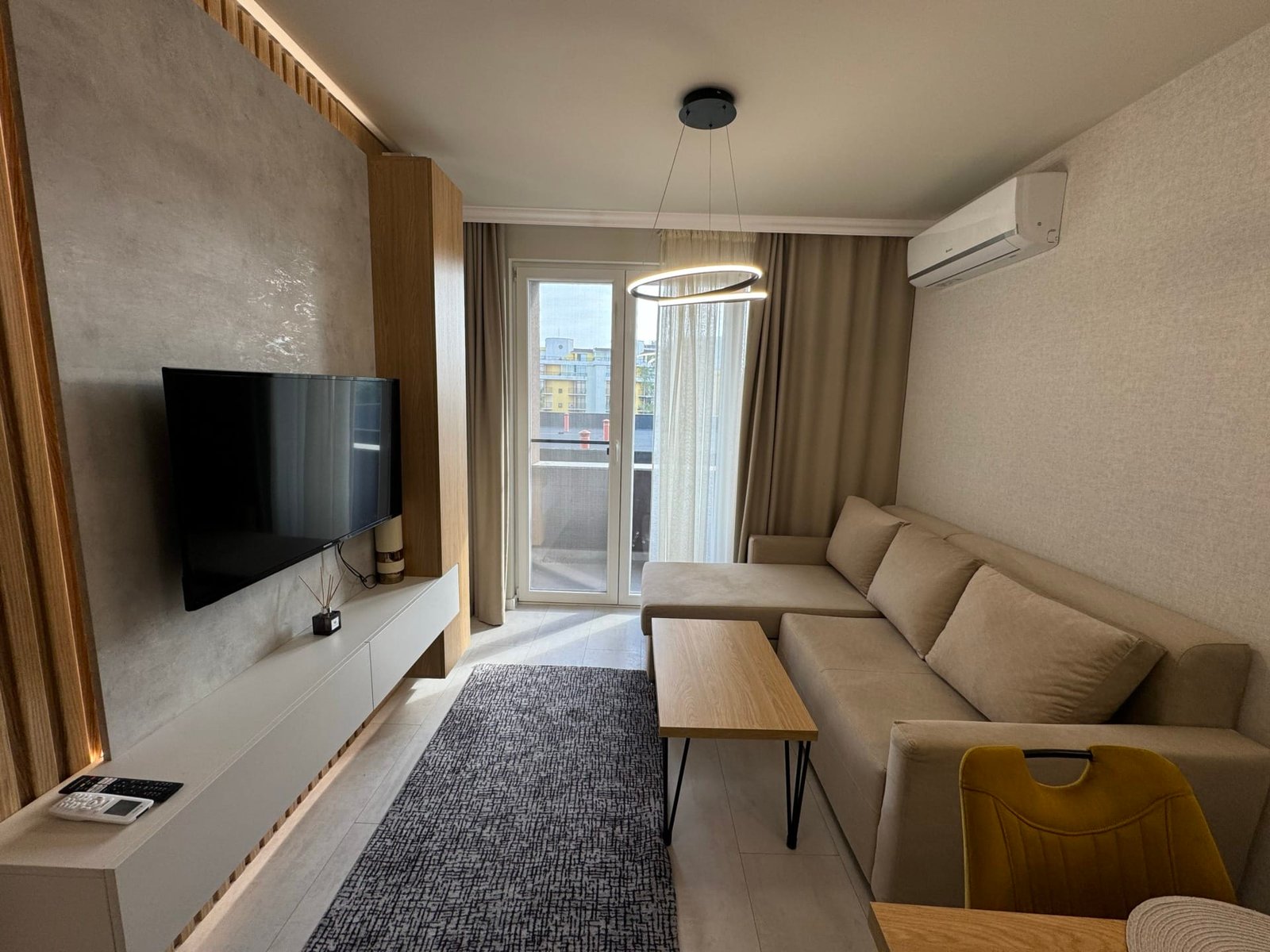 Современный интерьер квартиры с диваном, телевизором и балконом, идеальной для покупки недвижимости в Болгарии.