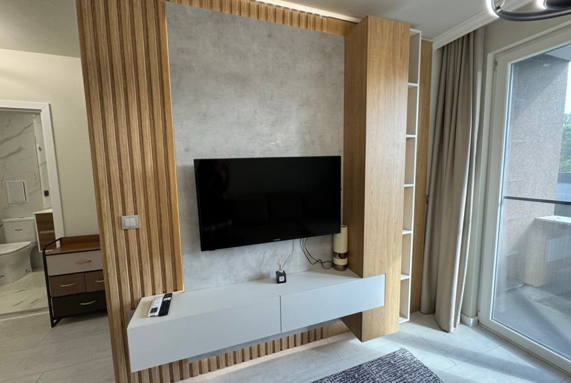 Современный интерьер квартиры в Болгарии с телевизором на стене, деревянными панелями и светлыми тонами.
