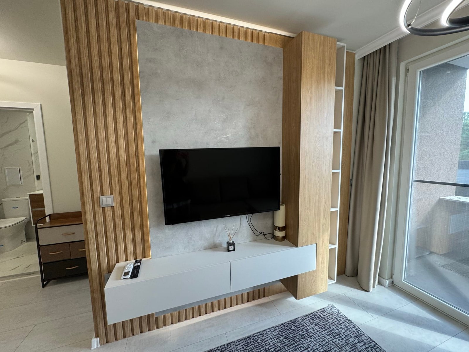 Современный интерьер квартиры в Болгарии с телевизором на стене, деревянными панелями и светлыми тонами.