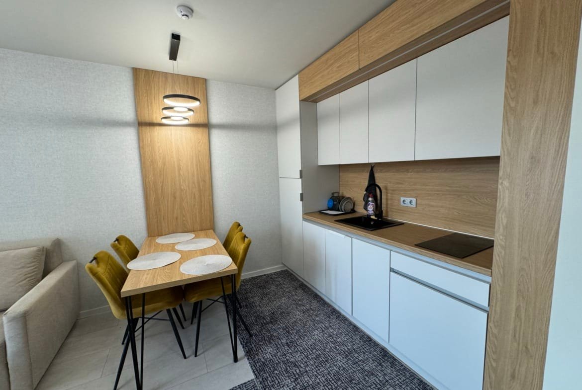 Современная кухня с обеденной зоной, светлым интерьером и деревянными элементами в квартире для продажи в Болгарии.