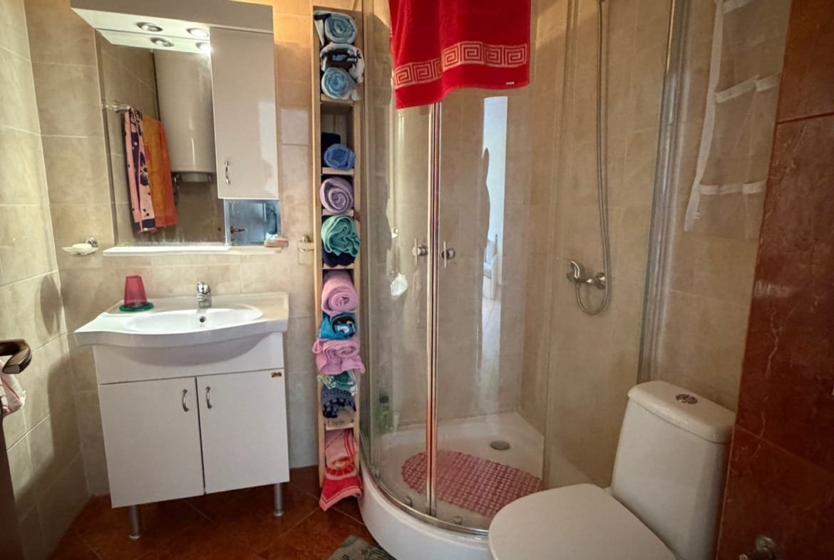 Современная ванная комната с душевой кабиной, туалетом, раковиной и полкой с полотенцами в мягких оттенках.