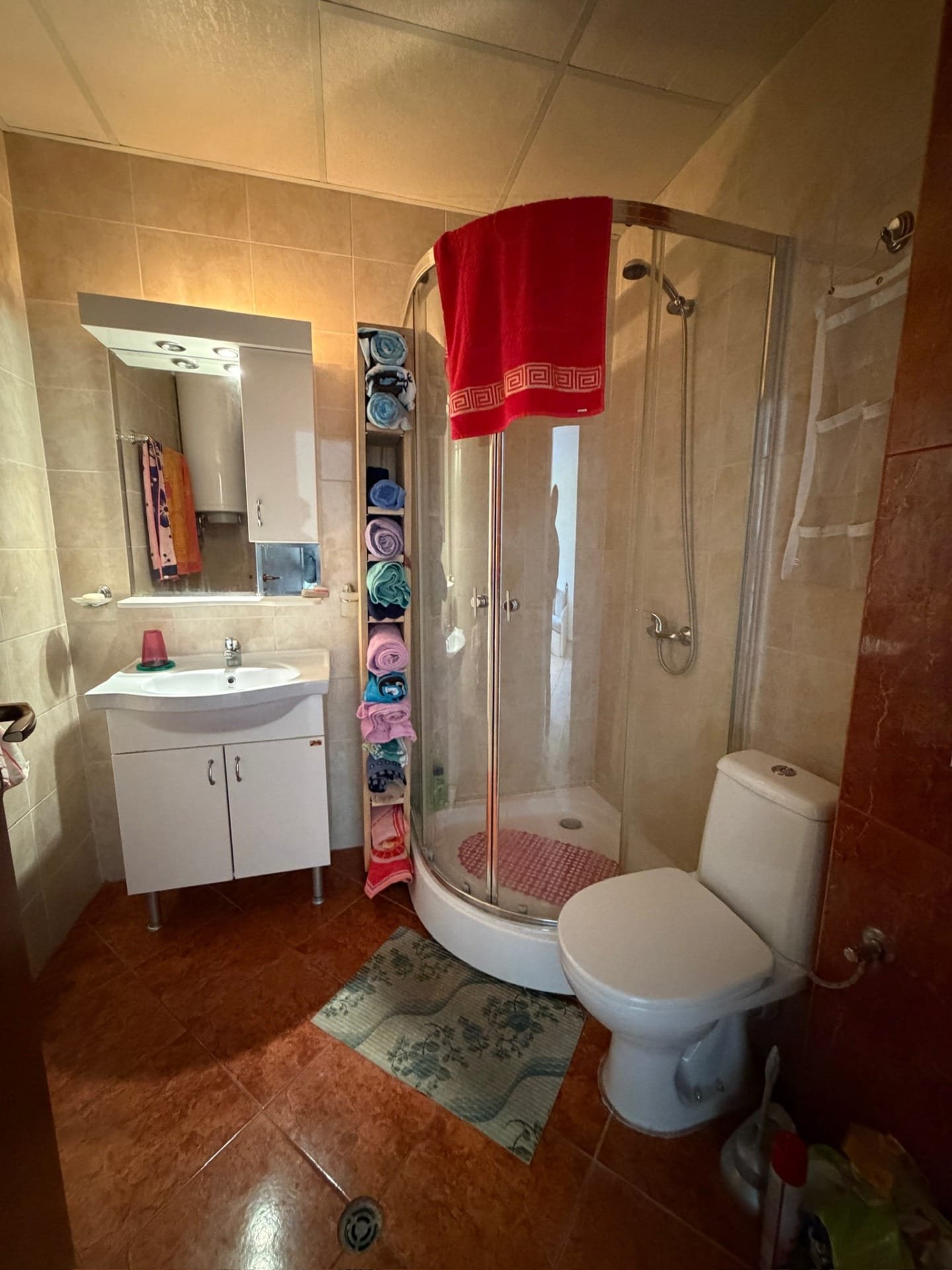 Современная ванная комната с душевой кабиной, туалетом, раковиной и полкой с полотенцами в мягких оттенках.