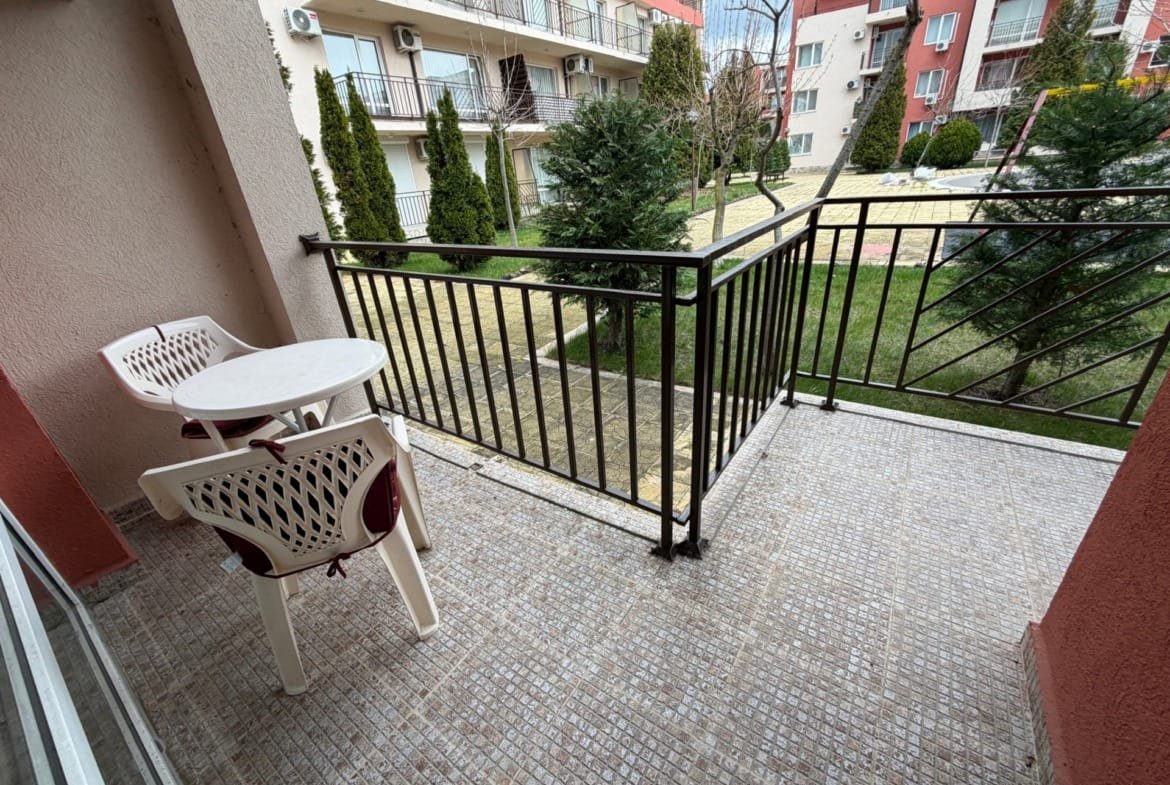 Балкон с видом на зелёный двор, столик и стулья для отдыха, идеальное место для покупки недвижимости в Болгарии.