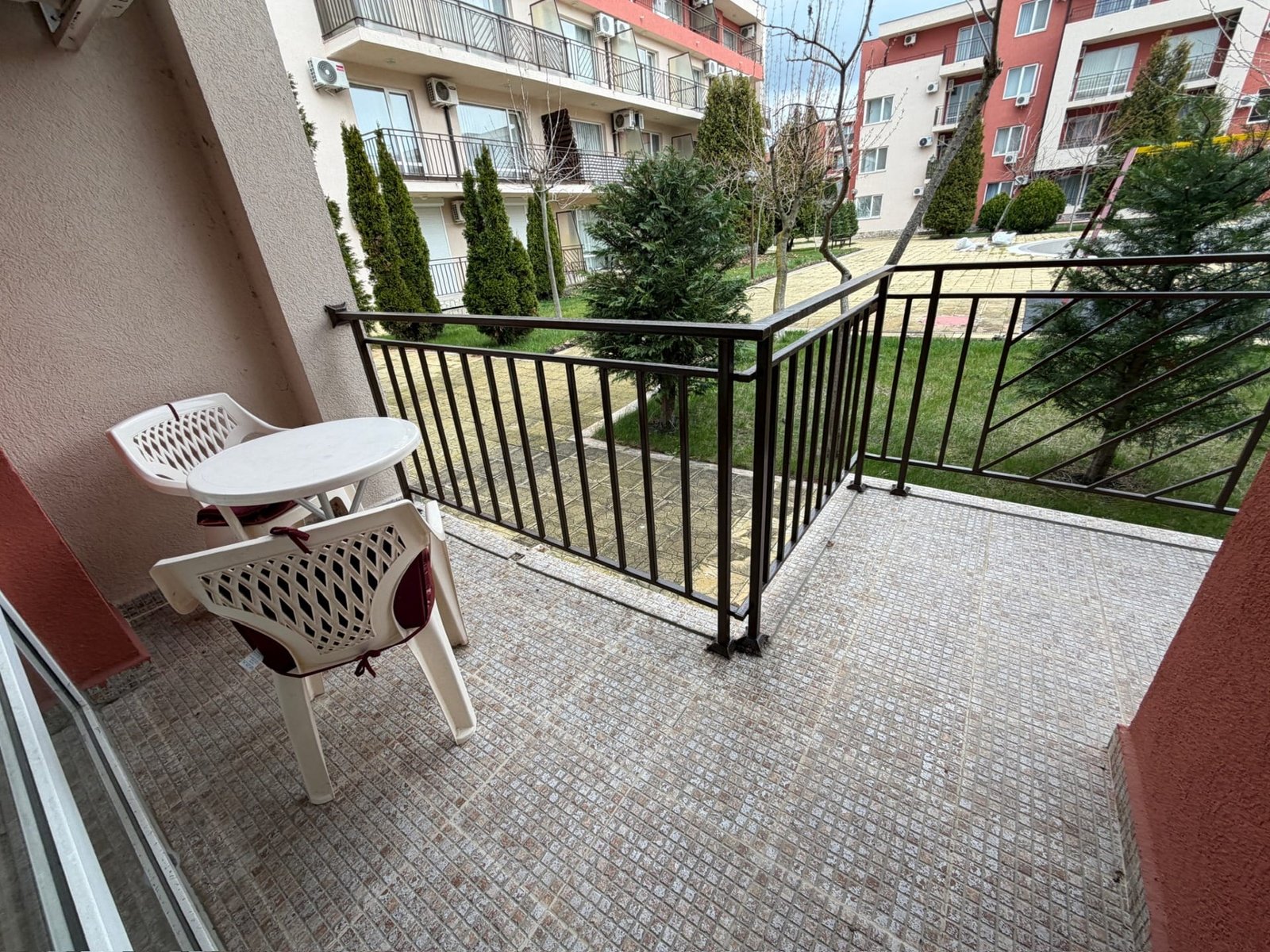 Балкон с видом на зелёный двор, столик и стулья для отдыха, идеальное место для покупки недвижимости в Болгарии.