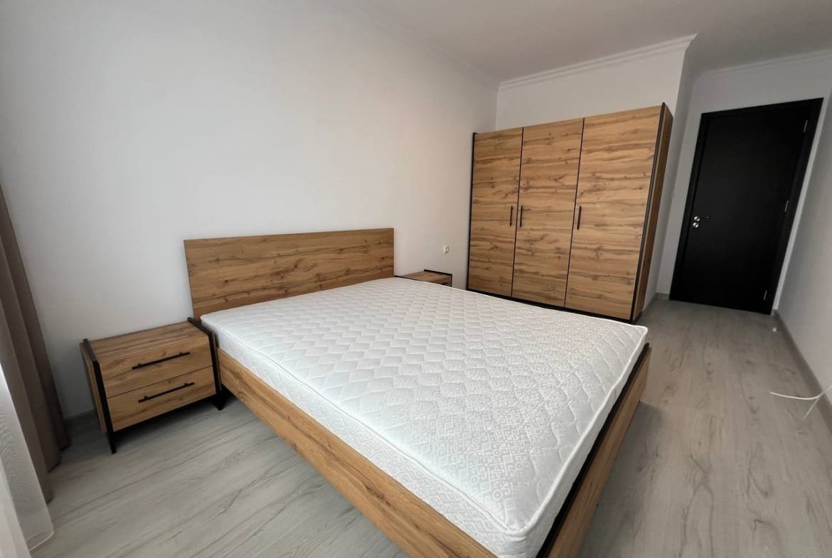 Современная спальня с деревянной мебелью, светлыми стенами и настенным шкафом, идеально подходит для покупателям недвижимости в Болгарии.