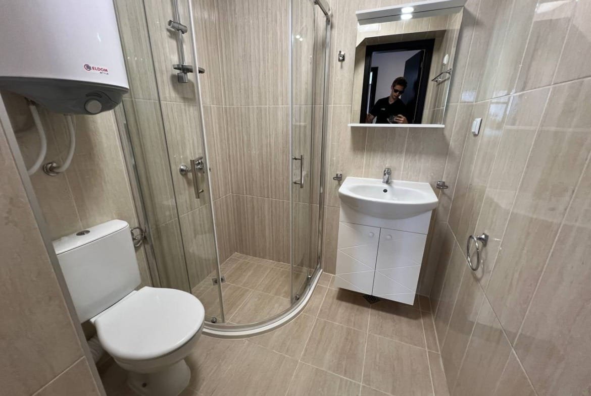 Современная ванная комната с душевой кабиной, унитазом и раковиной. Стены обклеены светлой плиткой, чистый и уютный дизайн.