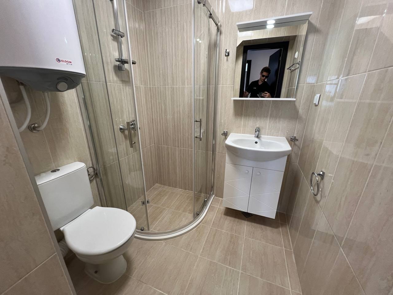 Современная ванная комната с душевой кабиной, унитазом и раковиной. Стены обклеены светлой плиткой, чистый и уютный дизайн.