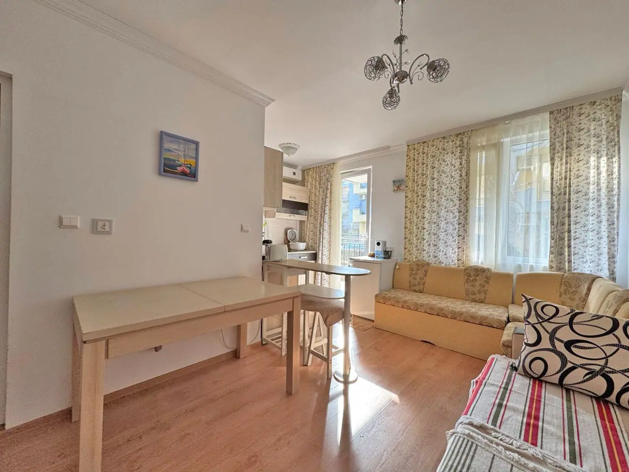 Современная гостиная с мягким диваном, столом и кухонной зоной, идеальная квартира для проживания в Болгарии.