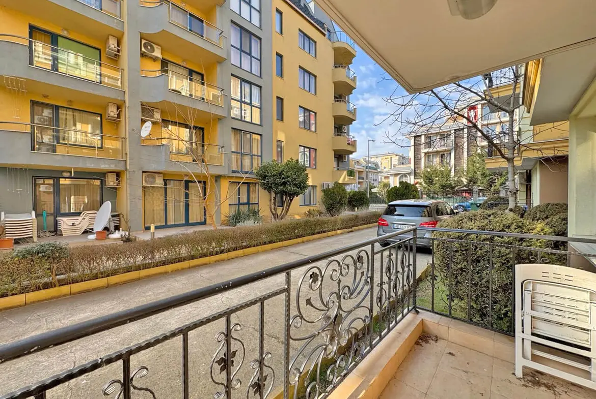 Терраса с видом на улицу в жилом комплексе, недалеко от апартаментов у моря в Бургасе, с зелеными насаждениями и парковкой.