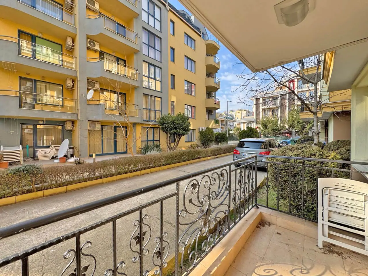 Терраса с видом на улицу в жилом комплексе, недалеко от апартаментов у моря в Бургасе, с зелеными насаждениями и парковкой.