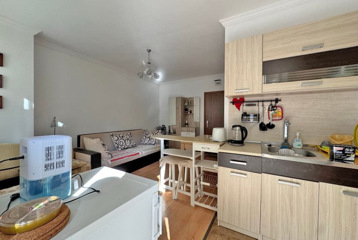 Современная кухня-студия с обеденной зоной и светлой мебелью, идеальна для апартаментов у моря в Болгарии.