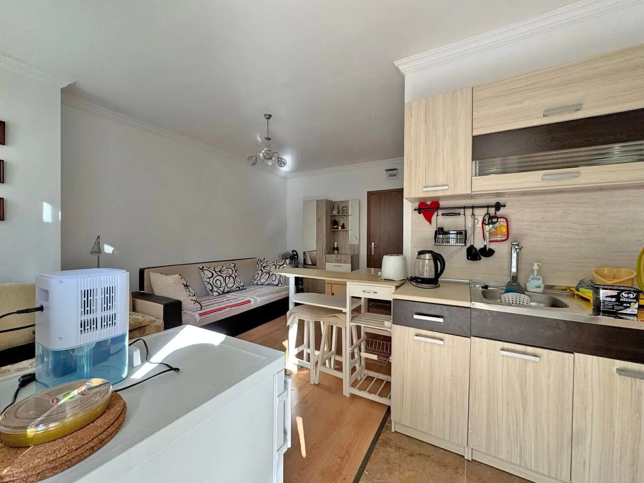 Современная кухня-студия с обеденной зоной и светлой мебелью, идеальна для апартаментов у моря в Болгарии.